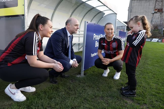 Image of two female Bohemian Football Club players, Dublin Bus CEO Billy Hann talking to a child